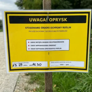 Żółta tablica ostrzegawcza z napisem Uwaga! Oprysk na drewnianym słupku przy wale nadodrzańskim w pobliżu Wyspy Opatowickiej